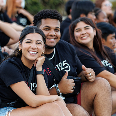 apu students sitting on the floor smiling and wearing black apu t-shirts