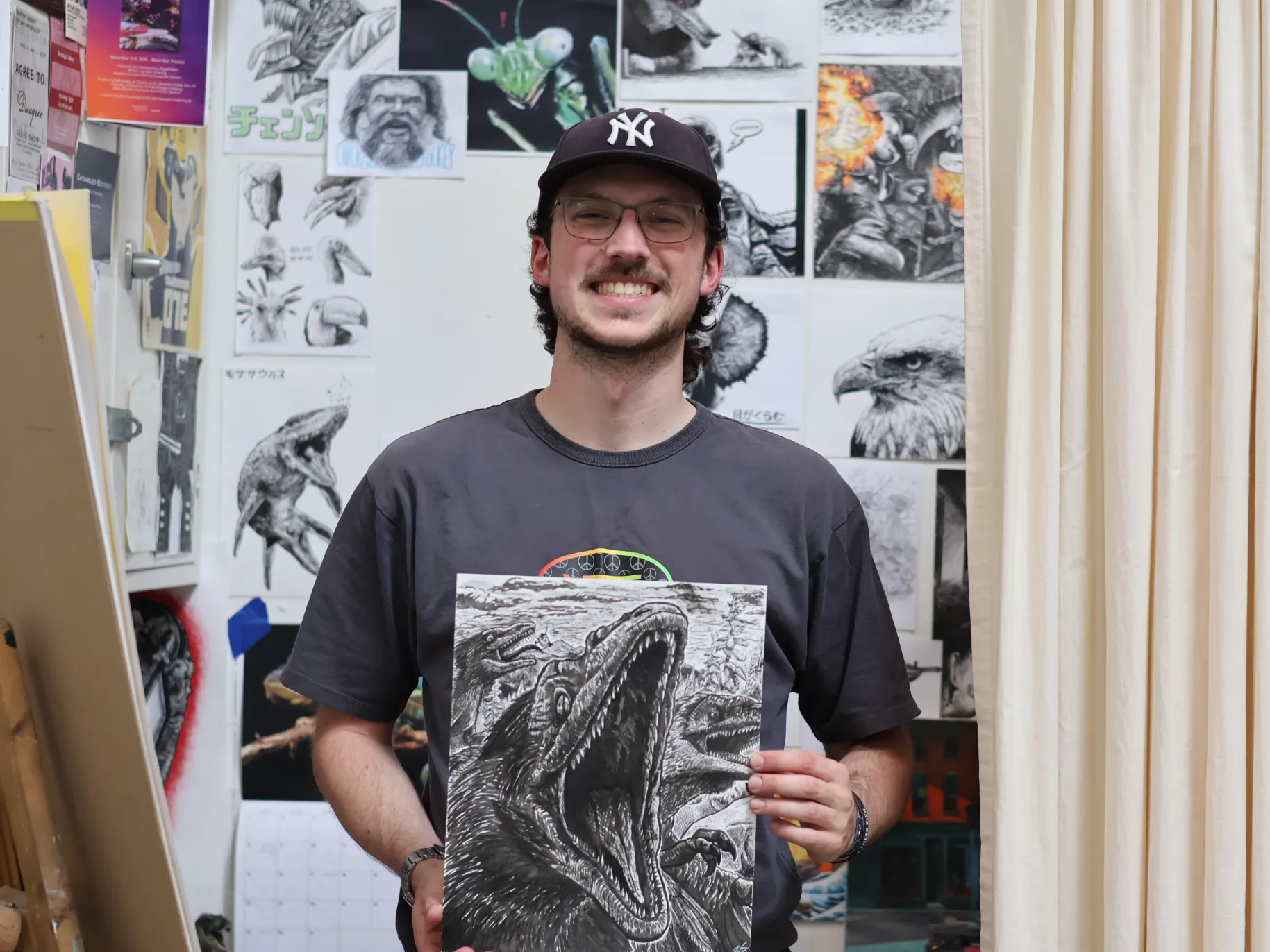Brandon Cooper holds an illustration of a dinosaur in front of his art studio.