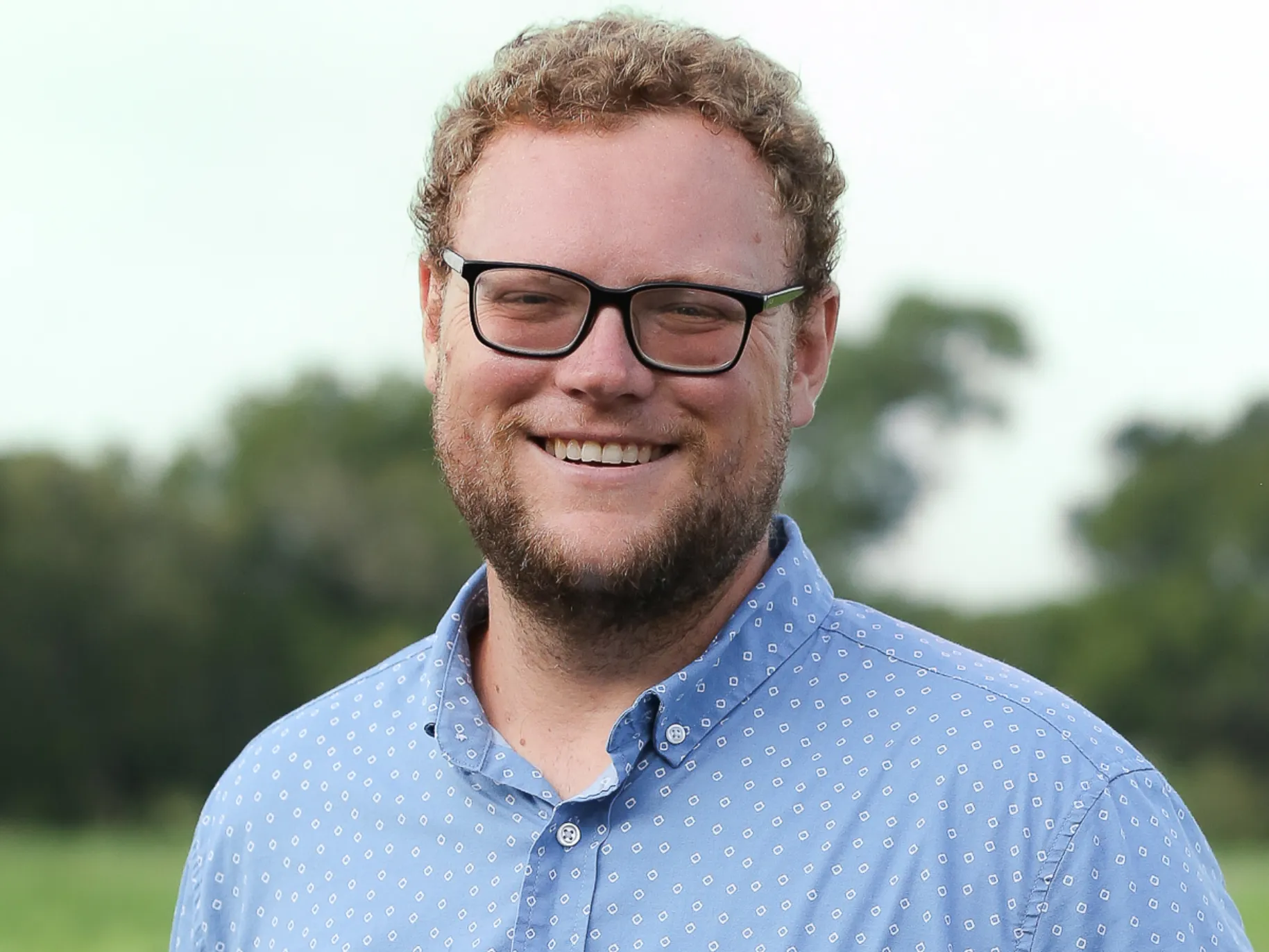 Man in Blue button-down stands smiling 
