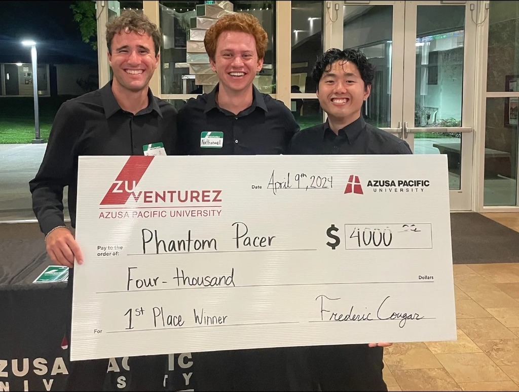 Three students stand smiling with oversized check for 4000