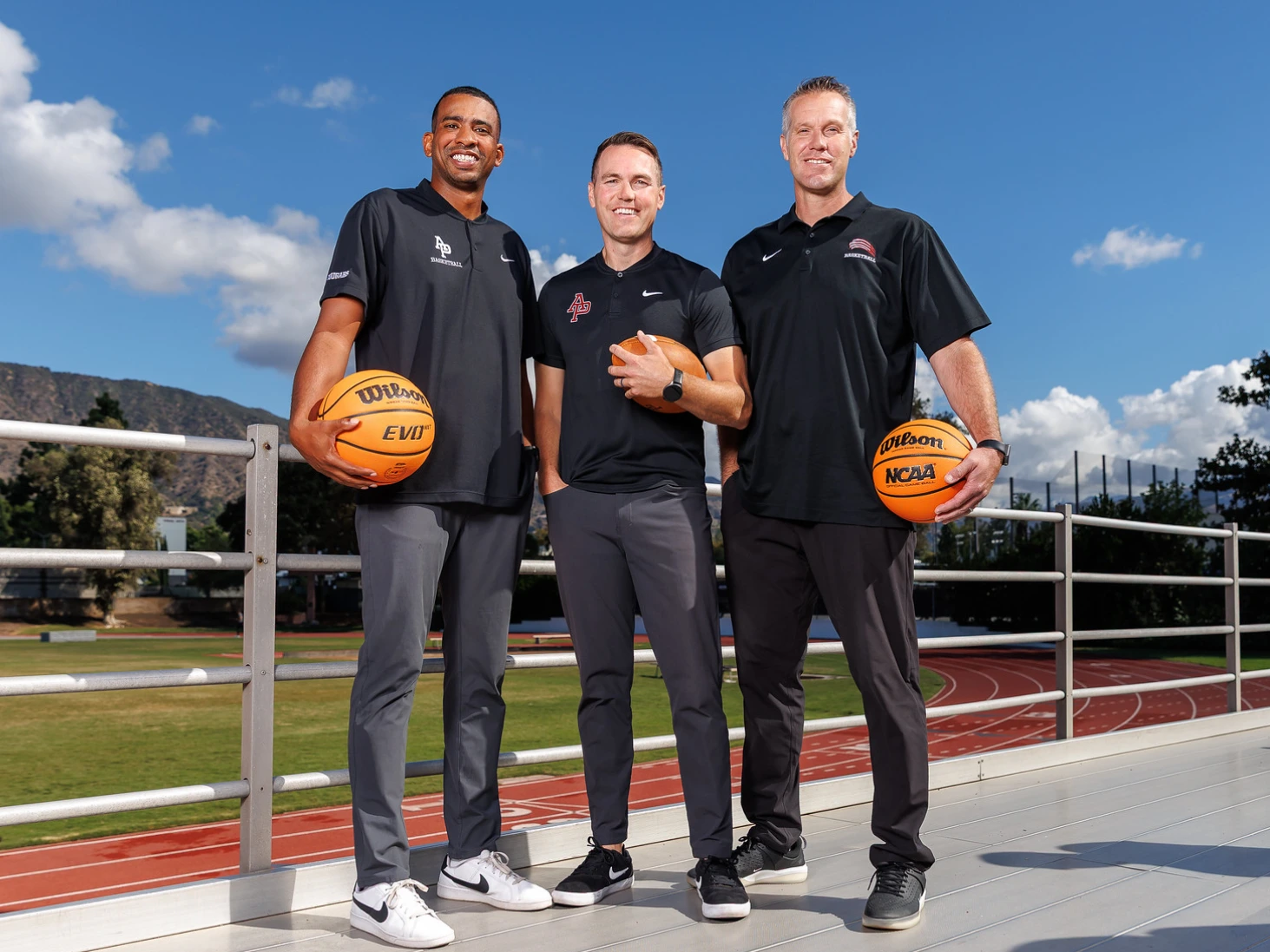 From left to right: APU's new head coaches— B.J. Porter, A.J. Parnell, and Dan Ploog smile in front of a field