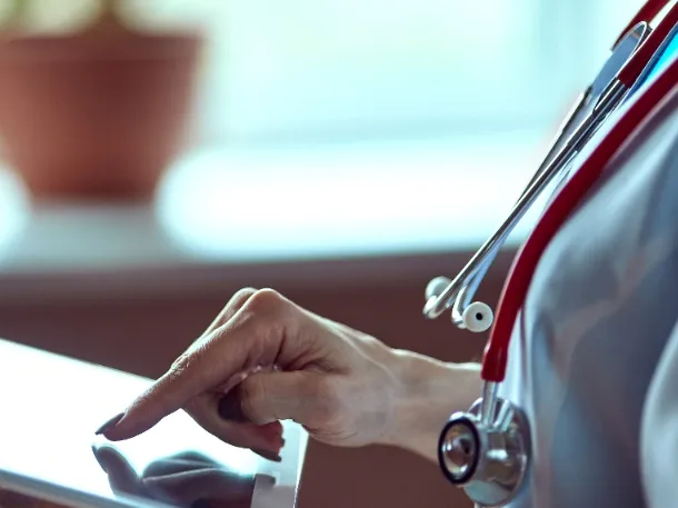 doctor's hand using an Ipad while wearing white and a stethoscope.