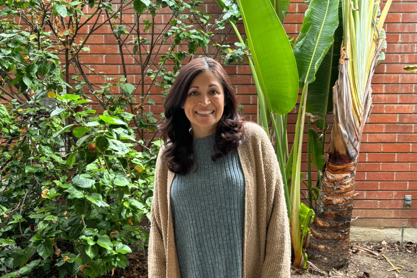 monica smiles outside her office near plants and a brick wall