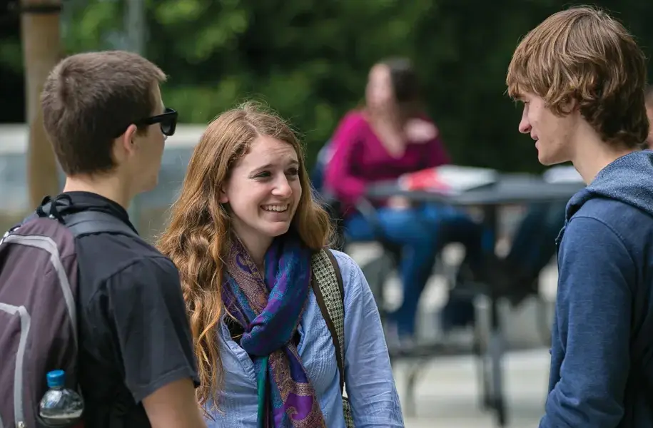 Three college students chatting and smiling together outdoors on campus.