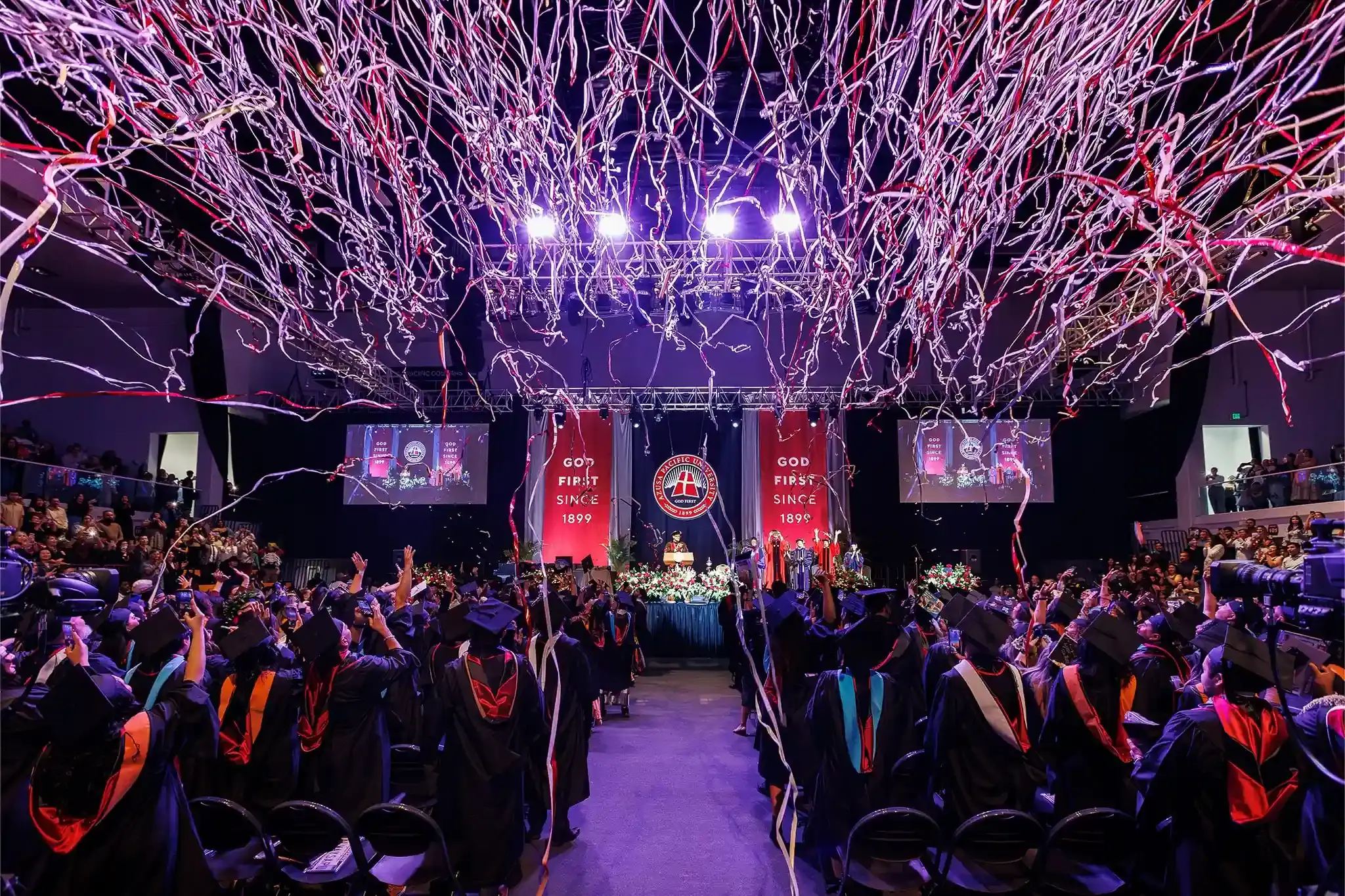 Graduates cheering under falling streamers at the APU commencement