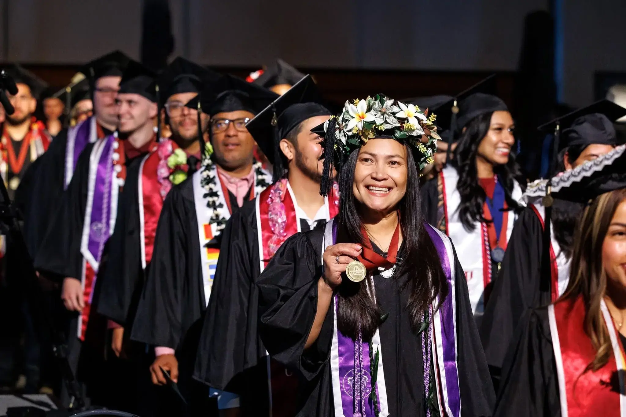 student smiling while holding a medal during commencement