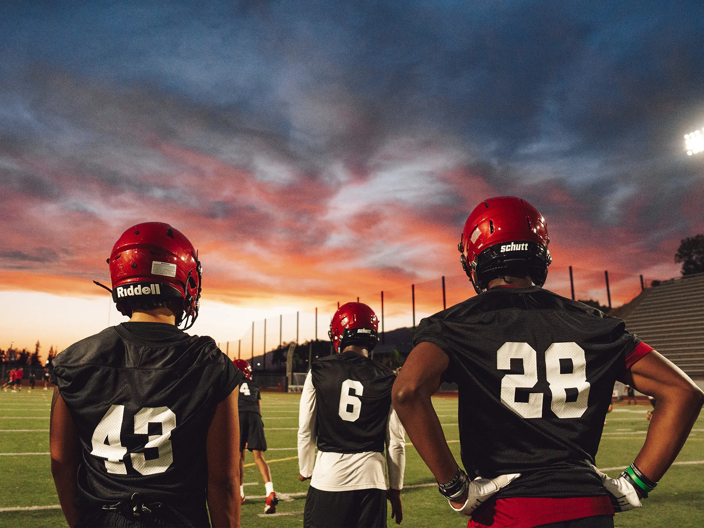 Three APU football players stand on the field during a sunset