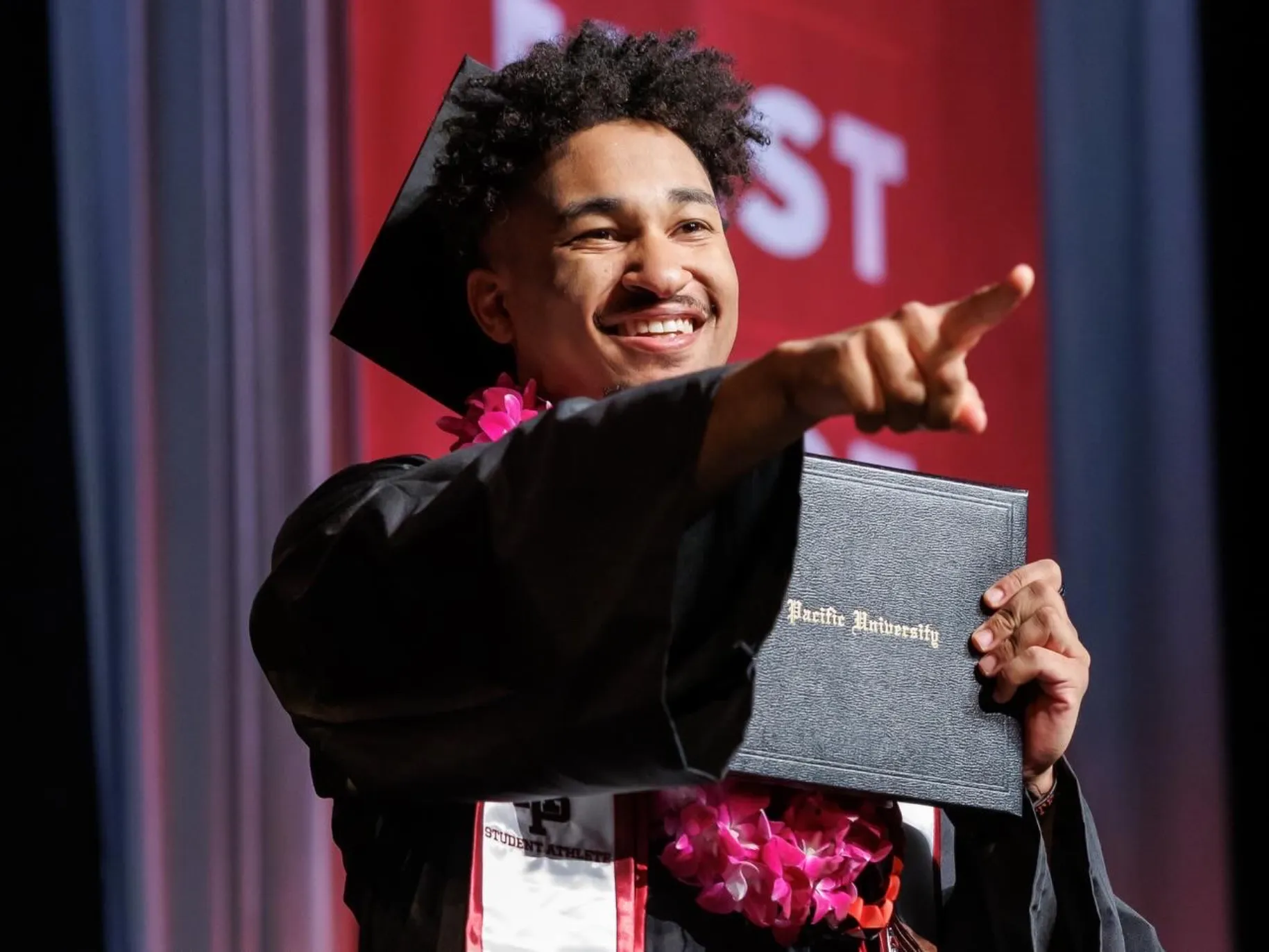 An APU graduate points at his family as he crosses the Commencement stage.