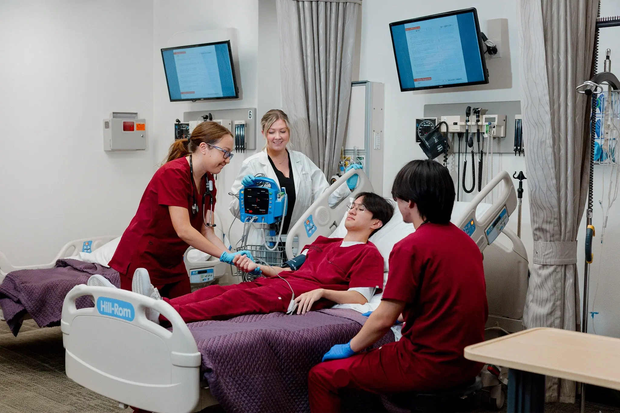 nursing students in brick red taking blood pressure of another student with their instructor guiding them