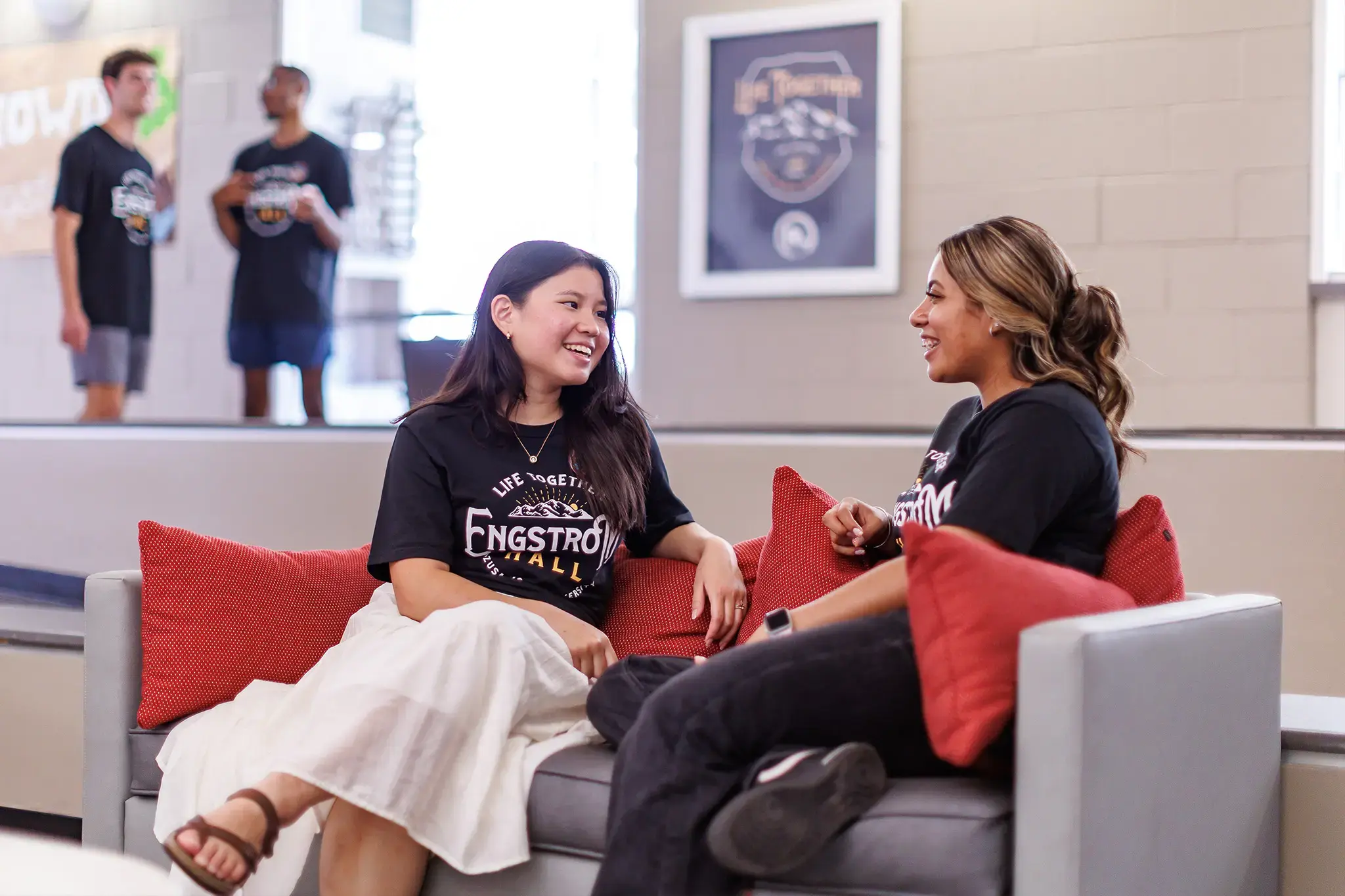 Two Azusa Pacific University students smiling and chatting on a couch in a campus lounge