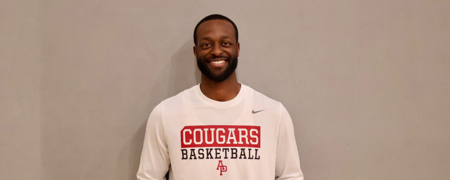 Dominique Johnson smiling wearing a white t-shirt with details in brick and apu logo