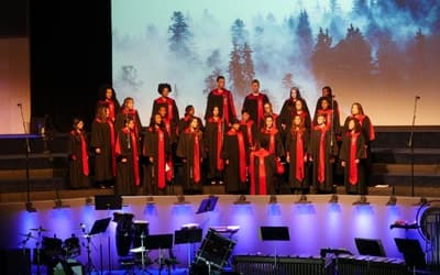 Image of the gospel choir performing in a stage wearing black gown with details in red.